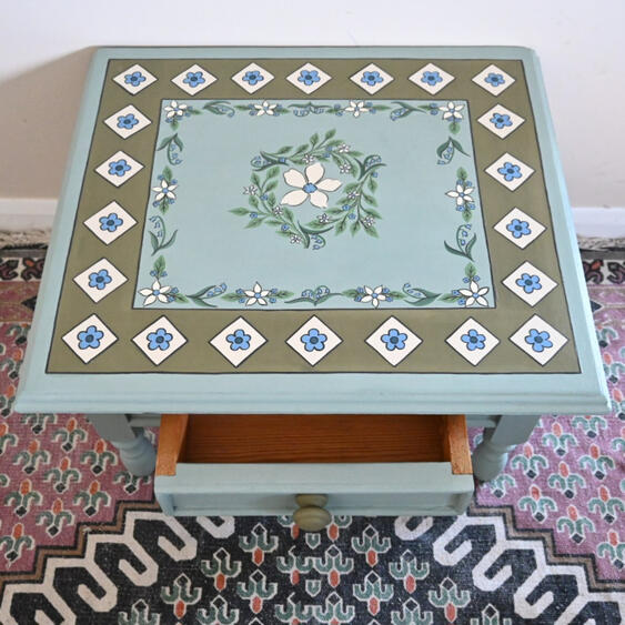 Painted wooden end table Hand-painted vintage side table in duck egg blue with floral hand-painted detail, one drawer, and turned legs. Refinished wooden side table with classic cottage style.