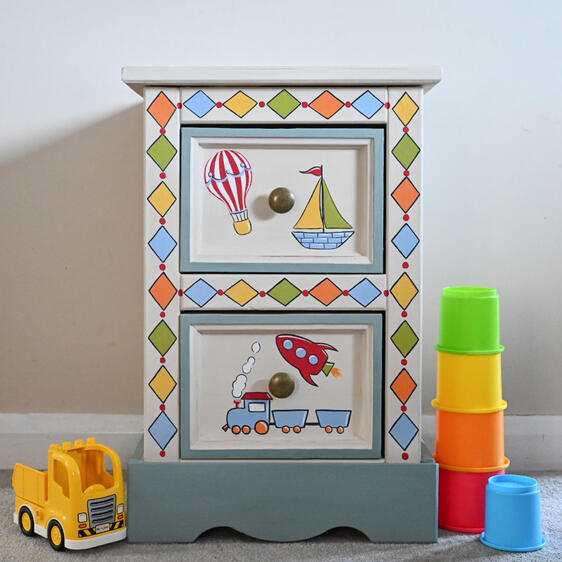 Boys bedside table A colourful children’s wooden storage unit with two decorated drawers, featuring hand-painted hot-air balloon, sailboat, rocket and train designs.