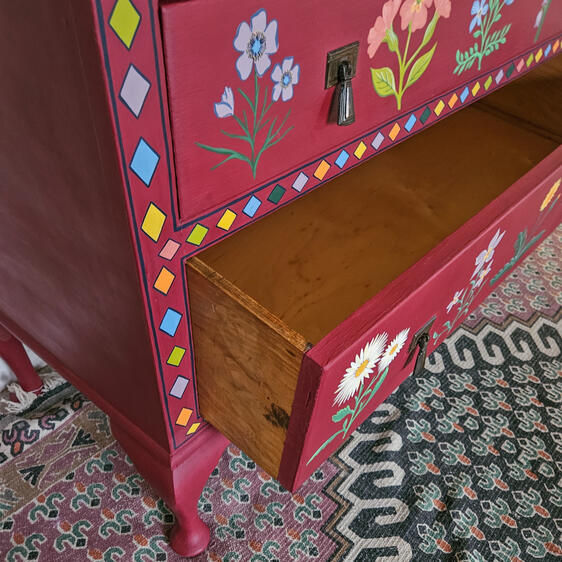 Hand-painted red wooden dresser with two drawers, featuring colorful floral folk-art motifs and decorative borders.
