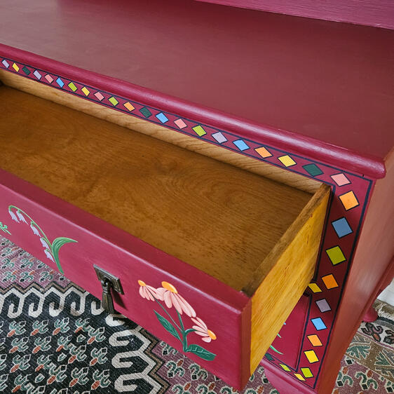 Hand-painted red wooden dresser with two drawers, featuring colorful floral folk-art motifs and decorative borders.