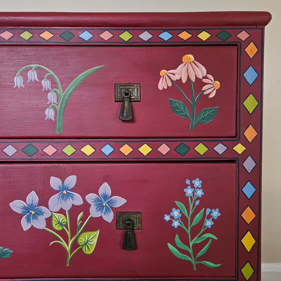 Hand-painted red wooden dresser with two drawers, featuring colorful floral folk-art motifs and decorative borders.