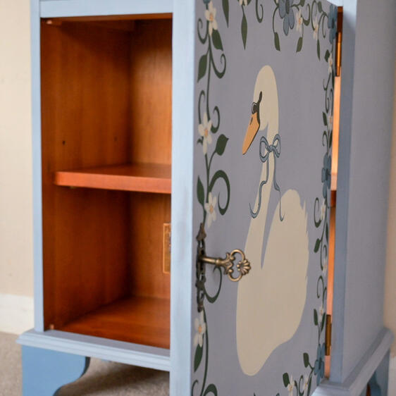 “Hand-painted blue wooden cabinet with swan design, floral detailing, vintage style bedside table or storage cupboard, unique upcycled furniture.”